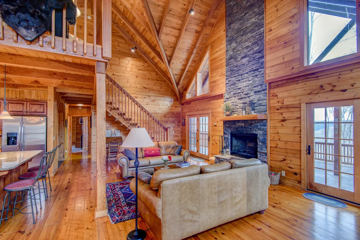 An inviting living area with a stone fireplace, comfortable seating, and a prominent wooden staircase, all bathed in soft daylight from large windows. This space blends warmth, openness, and architectural charm, perfect for both festive gatherings and quiet moments.