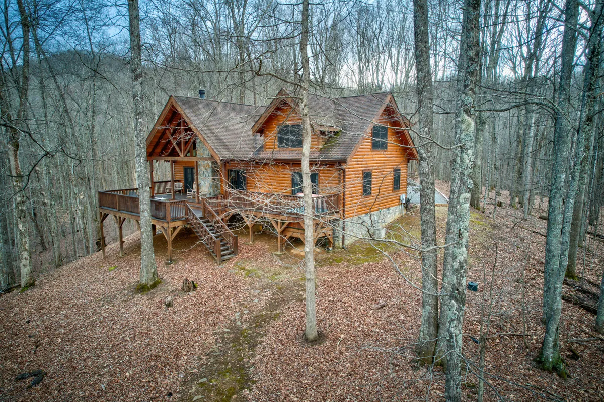 Here, the cabin is nestled among mature trees, with the welcoming porch and surrounding landscape inviting guests to explore. The setting hints at countless opportunities for hiking, wildlife observation, and enjoying the crisp mountain air.