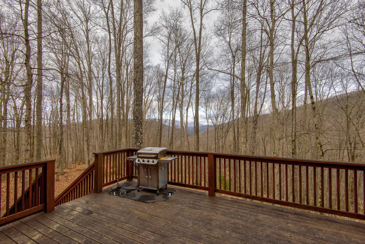 The photo showcases a spacious deck with a grill, seating area, and panoramic mountain views peeking through the trees. The deck is perfect for post-adventure relaxation, barbecues, or stargazing after a day spent hiking or skiing.