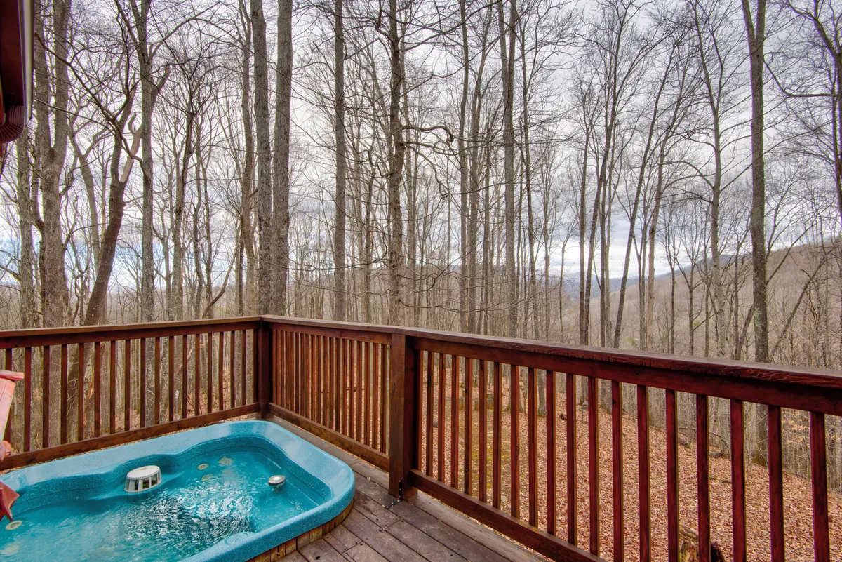 A close-up of the hot tub on the wooden deck, surrounded by trees with soft sunset lighting. The scene highlights the peacefulness and intimacy of enjoying a soak in nature, with hints of stargazing potential as evening approaches.