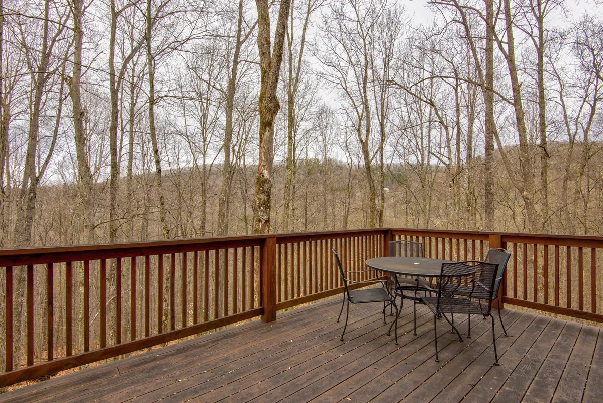 The photo captures a spacious wooden deck set among towering trees, featuring a table and chairs that invite guests to relax and immerse themselves in the mountain scenery. The deck is ideal for both morning coffee and evening relaxation under the stars.